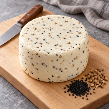 Niewędzony ser z czarnuszką i kolendrą 1,5 kg na jasnej desce z czarnuszką i okrągłymi nasionami kolendry.